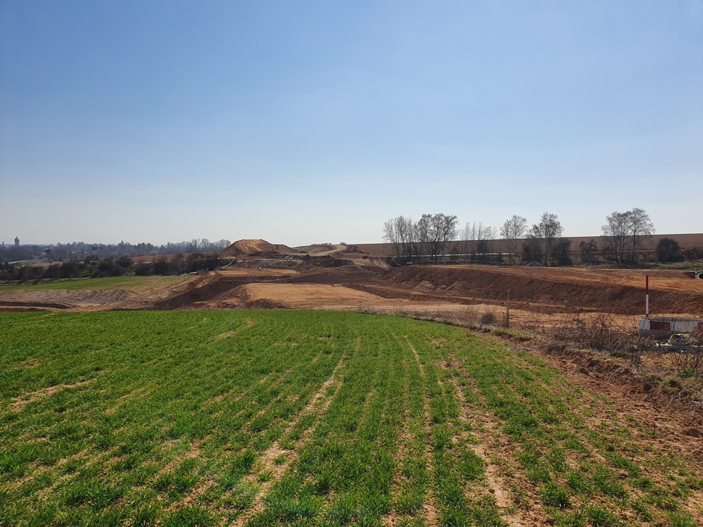 Pohled směr Hradec Králové přes původní vysoký násep, který byl jen konsolidačním a nyní je rozhrnutý a v "díře" usilovně dělníci armovali opěry. Kupa na dálnici v pozadí bude asi sloužit k vytvoření tělesa dálnice nad novým mostkem. Za mnou je v hlubokém zářezu odbočná větev směr OK u Hořenic, na pravém okraji fotky se v náznaku připojuje větev od této OK.