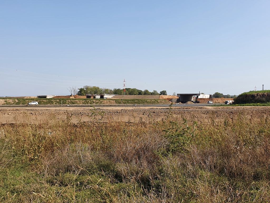Křižovatka s I/35. Celá stavba je nad úrovní okolního terénu, takže se nedá pořádně vyfotit. Vpravo mimo záběr je hotový most nad polní cestou z Břízy do pole, Dále je vpravo mimo záběr hotový jižní most nad kruhovým objezdem, první viditelný most zprava je severní most nad kruhovým objezdem, druhý viditelný trojmost zprava je most nad ramenem Pha - Jičín, poslední viditelný most zcela vlevo je most přes žel. trať HK - Jičín. Pohled je ve směru na PL. Dále je hotový středový pilíř na ramenu Pha - Jičín nad silnicí I/35. V křižovatce je položeno dost asfaltu, ale asi se jedná jen o budoucí provizorní komunikaci, protože pro účely křižovatky nedává smysl.